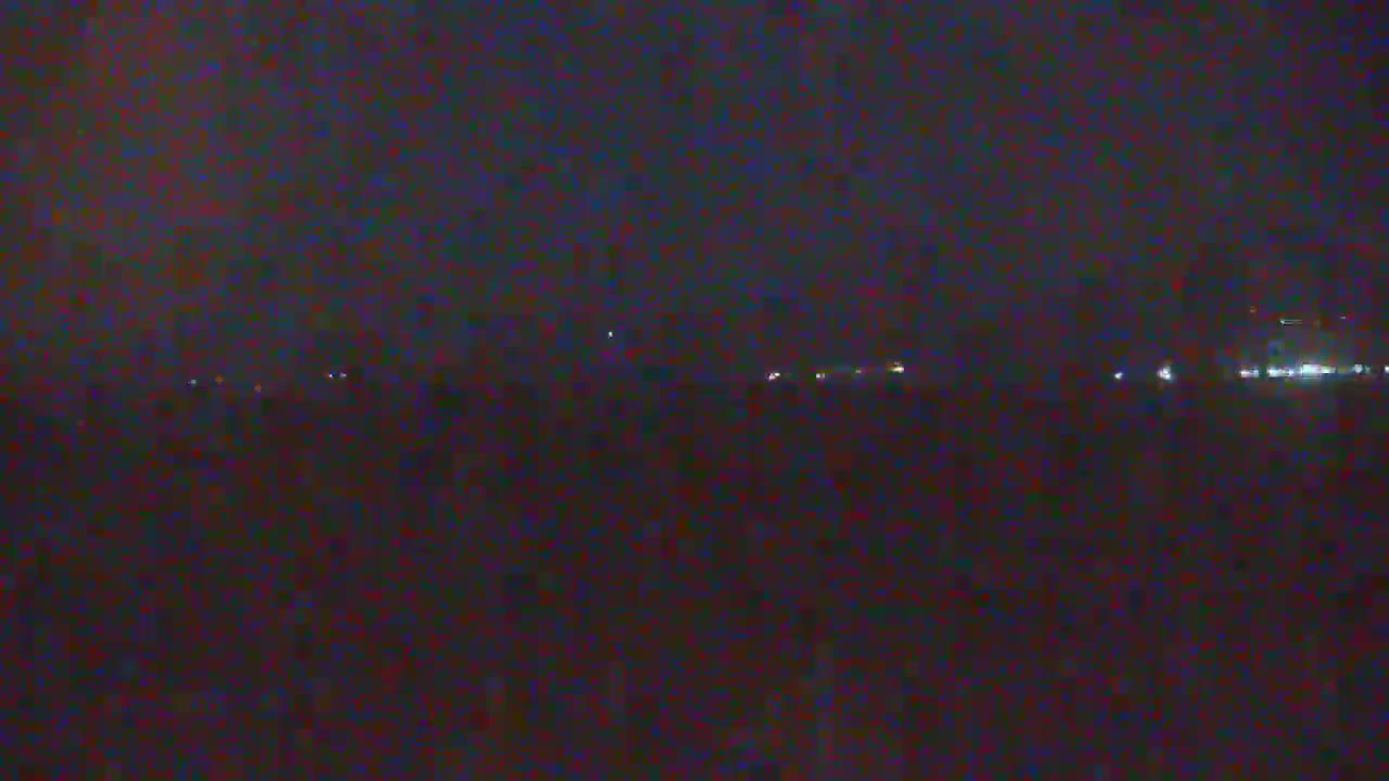 A dark, nighttime scene shows a distant line of lights possibly from a town or city under a mostly clear sky.