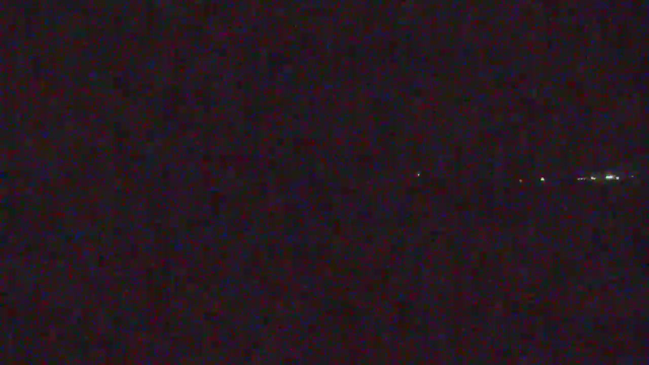 A very dark nighttime landscape shows a few distant lights clustered on the horizon under clear weather conditions.