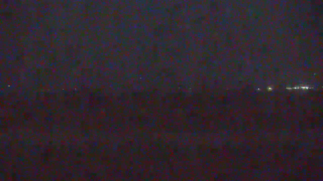 The very dark and grainy image shows faint, scattered lights along a distant horizon at night under apparently clear or mildly cloudy skies.