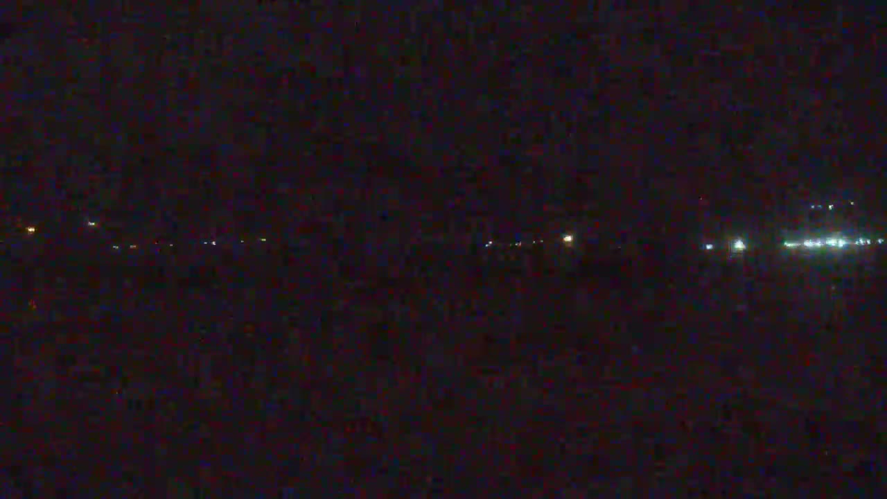 A very dark and grainy outdoor nighttime scene displays a horizontal line of distant, blurry lights, suggesting clear conditions.