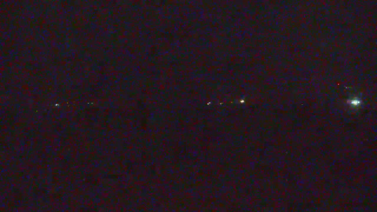 A very dark and grainy outdoor nighttime scene displays a horizontal line of distant, blurry lights, suggesting clear conditions.
