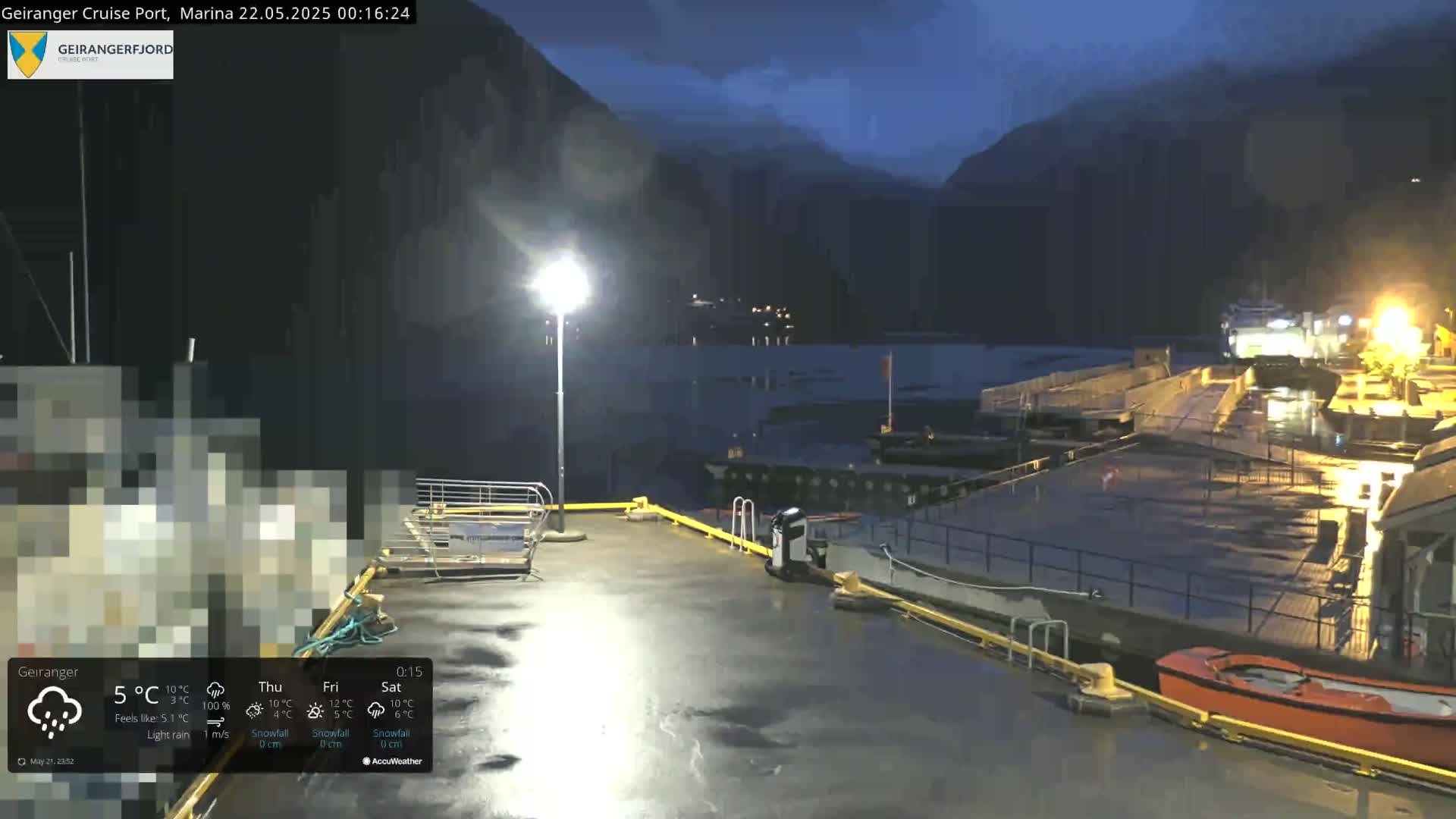 A nighttime view of a wet cruise port marina, illuminated by lights, with boats docked and dark mountains in the background under a dark sky.