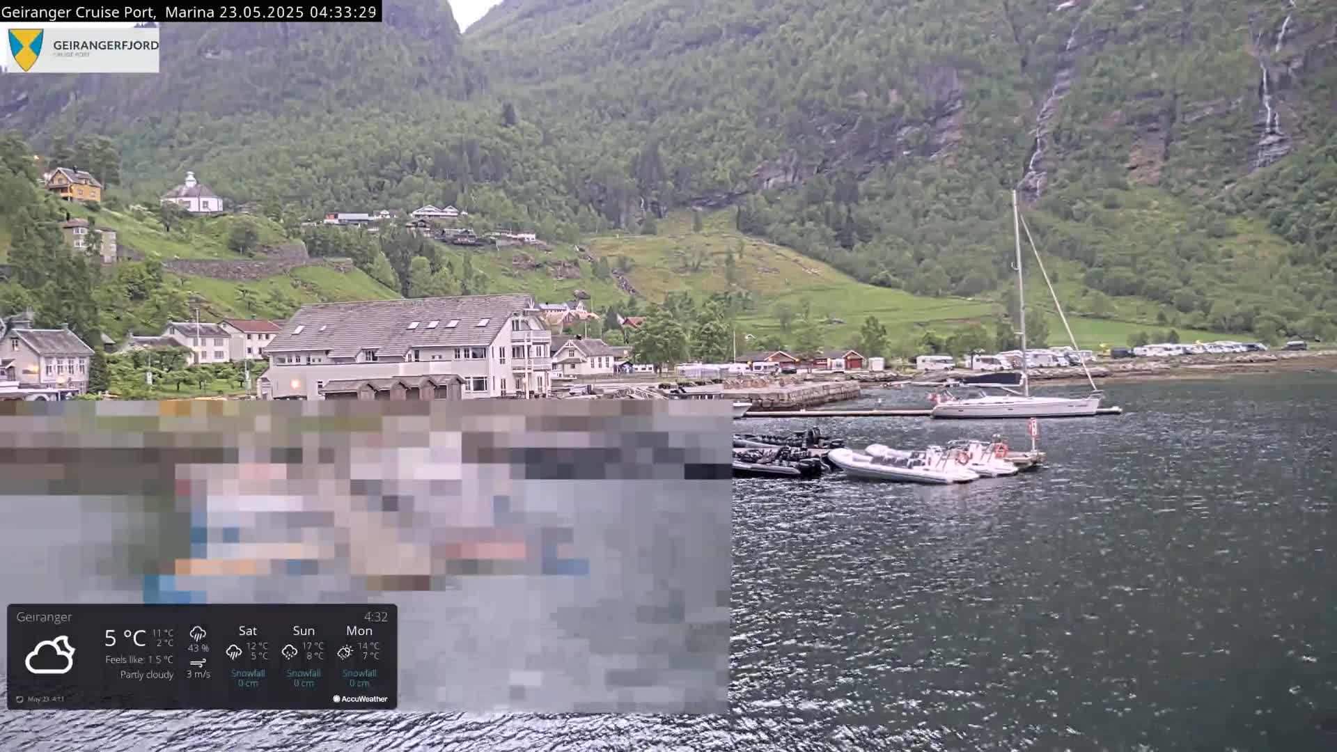 A partly cloudy harbor scene with several boats, including a sailboat and inflatable motorboats, is nestled at the base of a steep, green mountainside under a light rain.