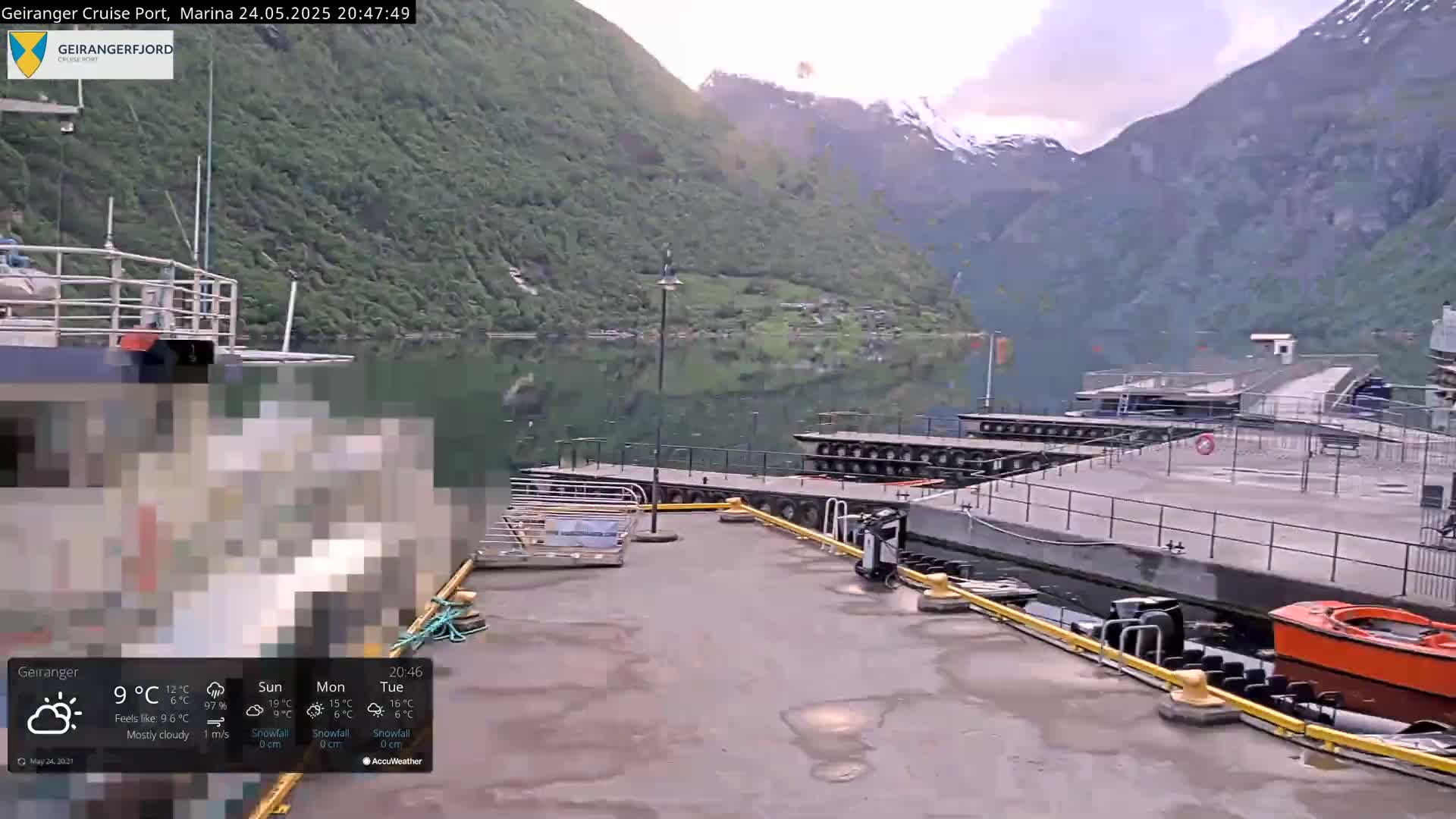 A mostly cloudy evening scene shows a cruise port marina situated beside a fjord, with mountains rising in the background.