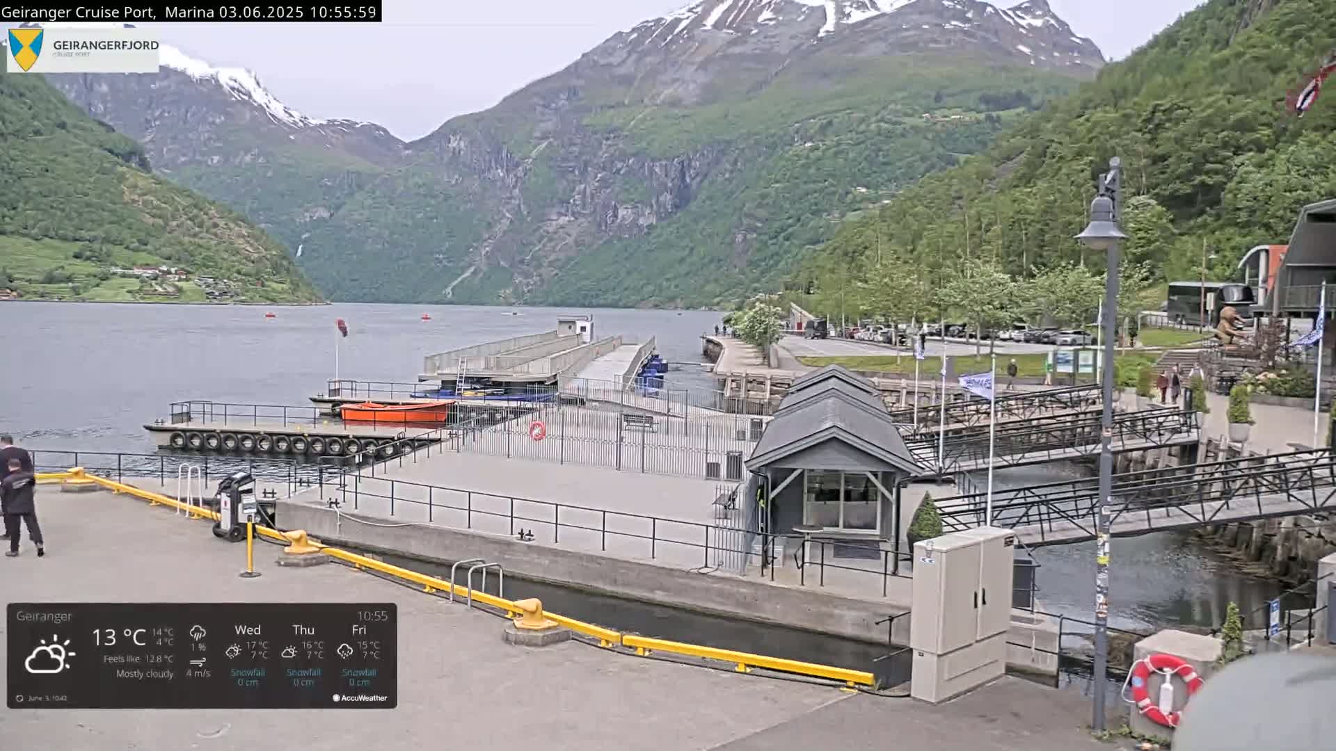 A mostly cloudy day at a marina nestled between mountains, with calm water and several small boats docked.
