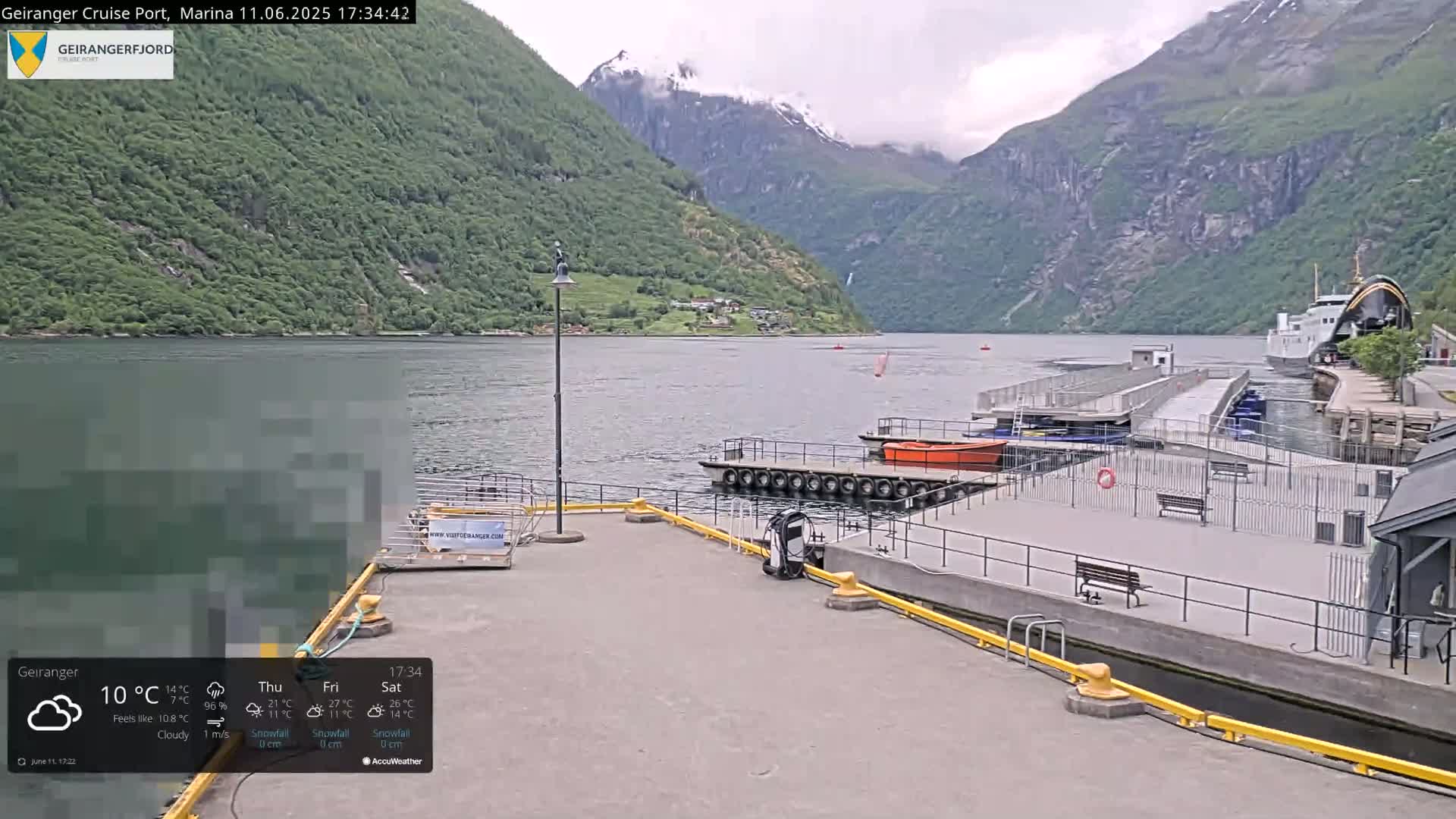 A cloudy day at a harbor in a fjord, with mountains in the background, boats docked at a pier, and a ferry in the water.