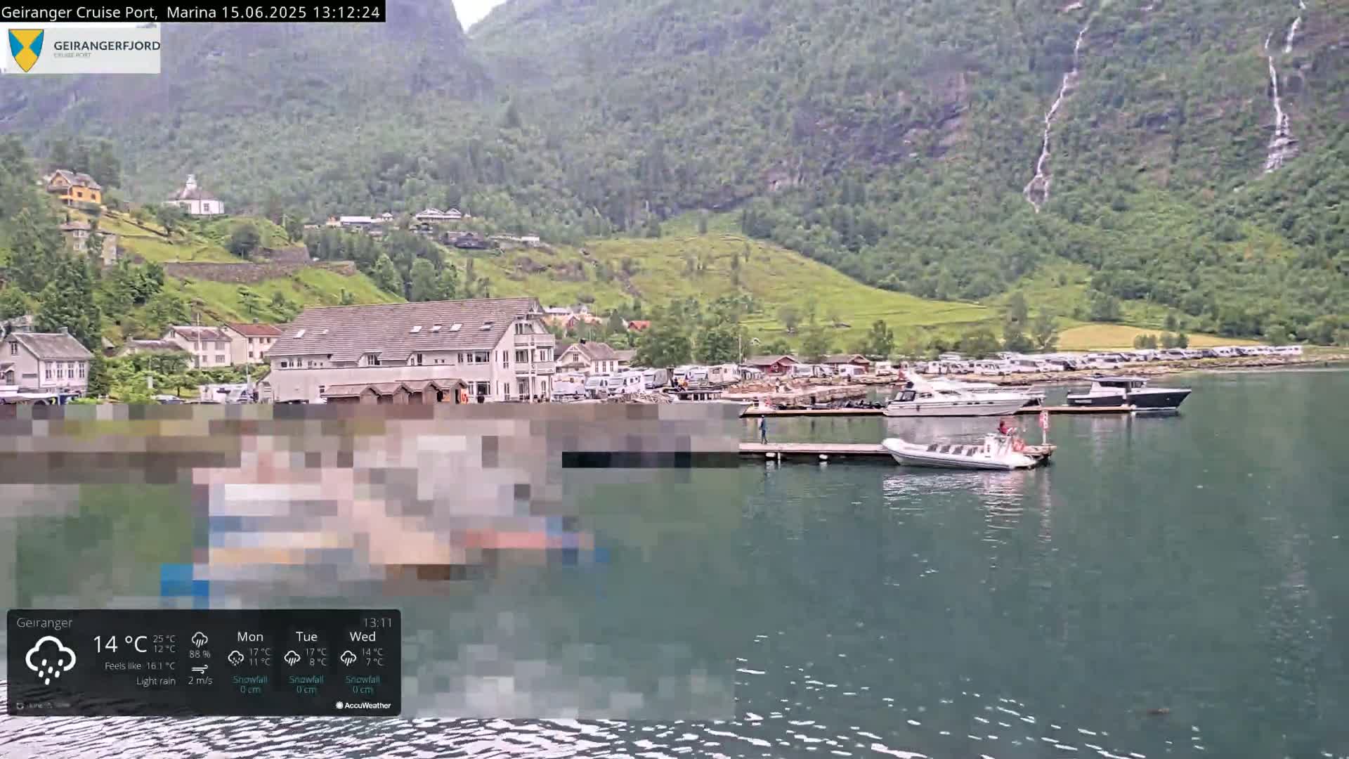A rain-swept harbor town nestled against a verdant mountainside with several boats moored at a dock.