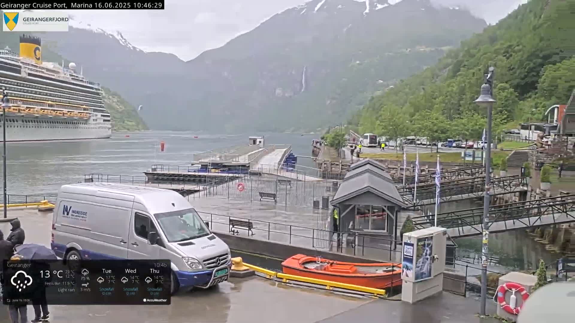 A cruise ship is moored near a marina in a fjord surrounded by rain-soaked mountains, with a van and small orange boat visible at the dock.