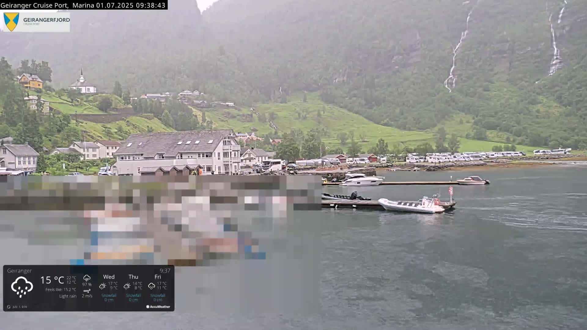 A rain-soaked marina scene shows a small town nestled against a lush, green mountainside with several boats docked, under a light rain.