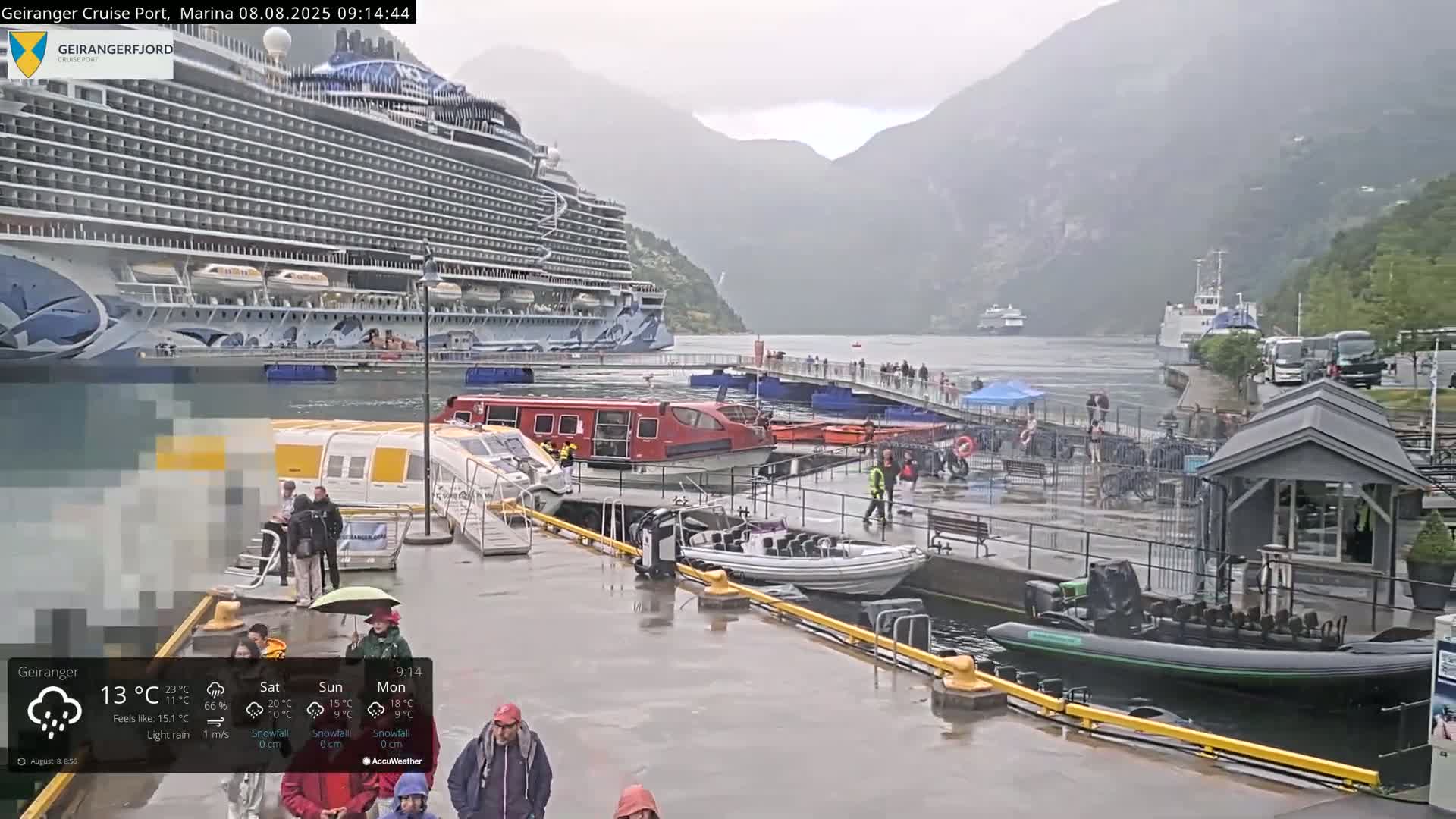 A large cruise ship is docked at a port in a fjord during light rain, with smaller boats and people present on the wet dock.