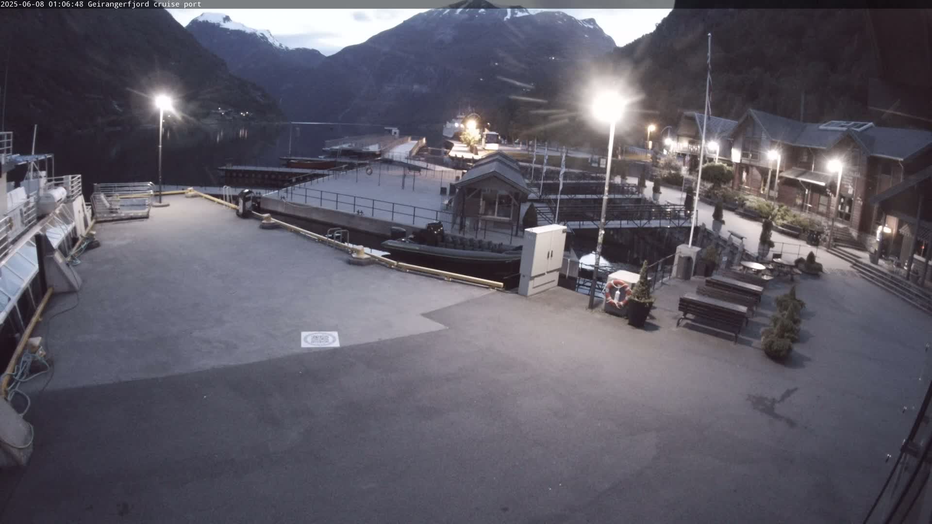 A cruise ship port at twilight, with calm water, mountains in the background, and a few boats docked.