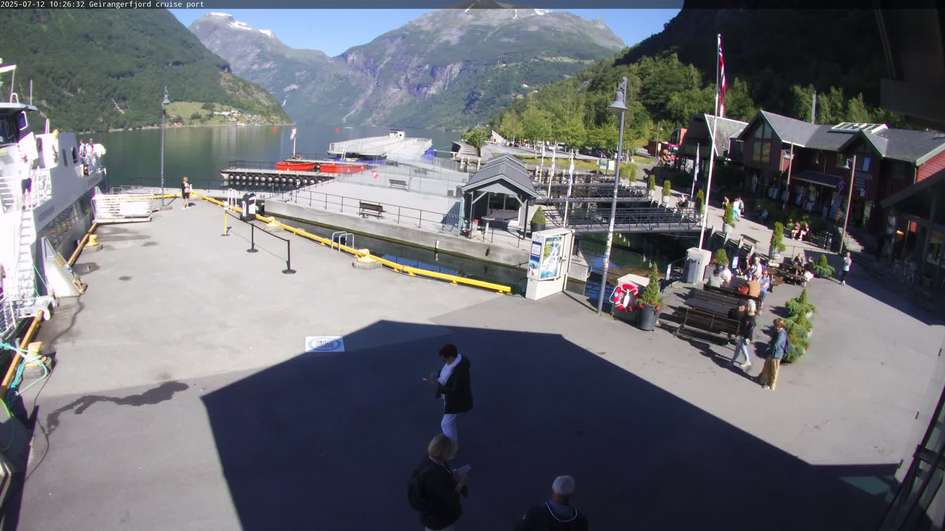 A cruise ship is docked at a port nestled between mountains on a sunny day.