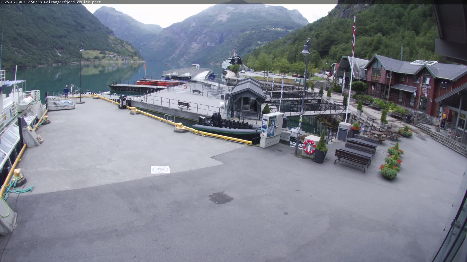 A cruise port sits on a calm body of water next to steep, green mountains under a mostly clear sky.