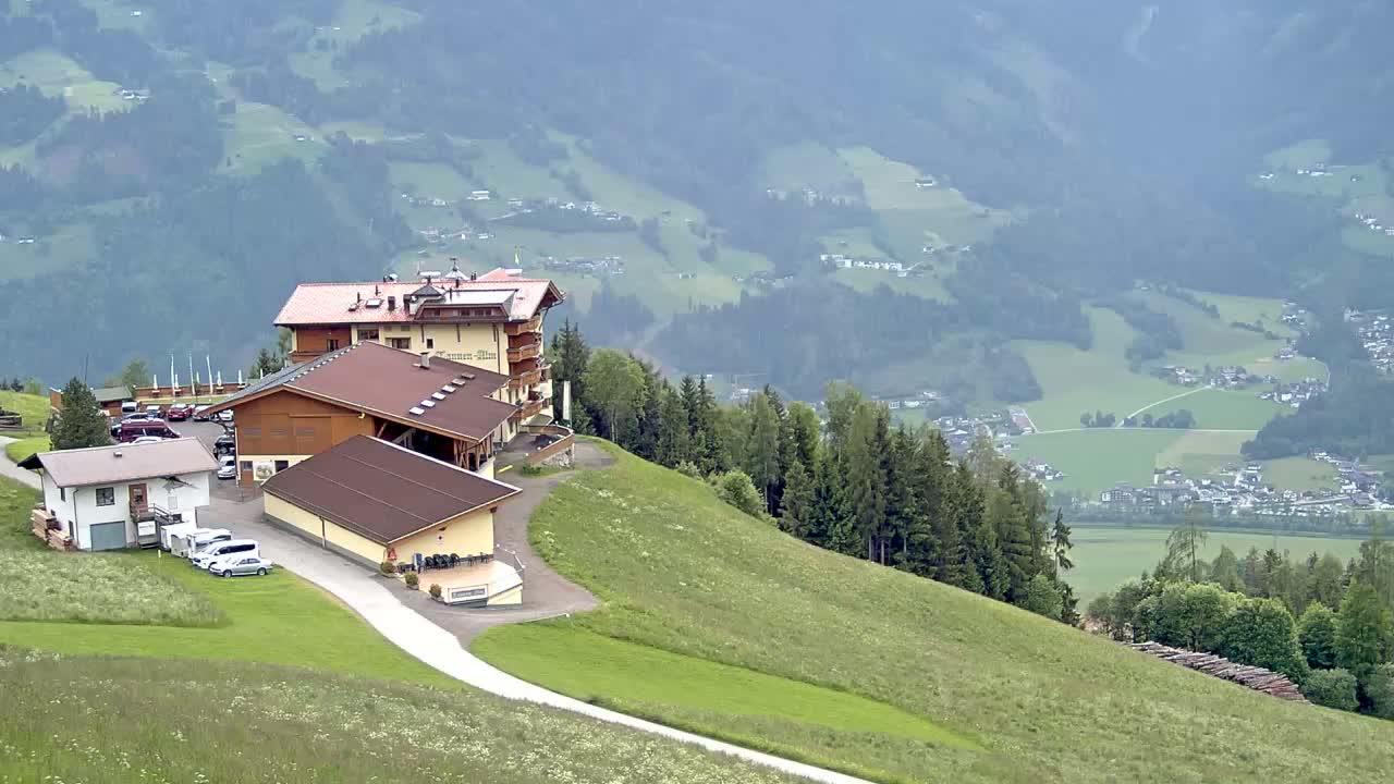 A hotel and several outbuildings sit atop a grassy hill overlooking a hazy valley dotted with small villages and forests.