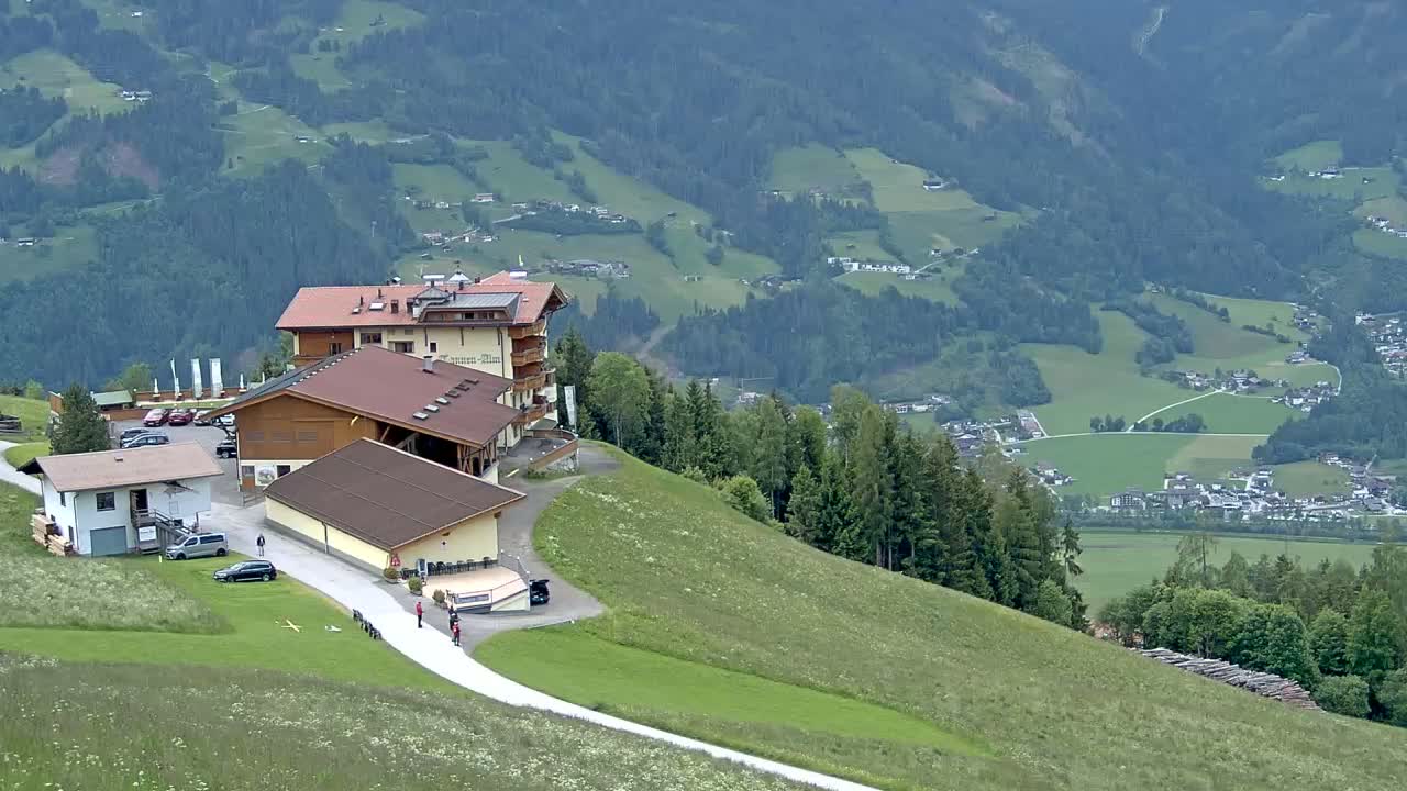 A mountaintop hotel complex overlooks a valley of green fields and villages under a cloudy sky.