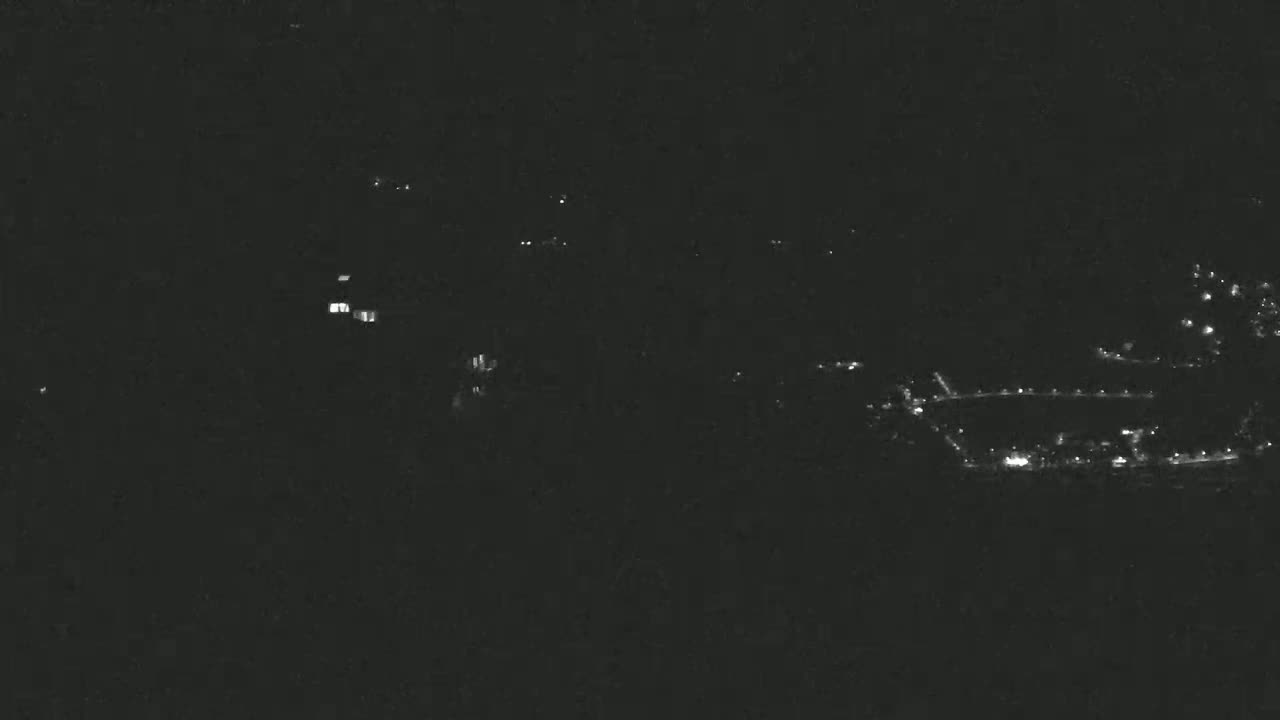 A nighttime long shot of dimly lit buildings and structures, possibly a town or small city, under a dark, clear sky.