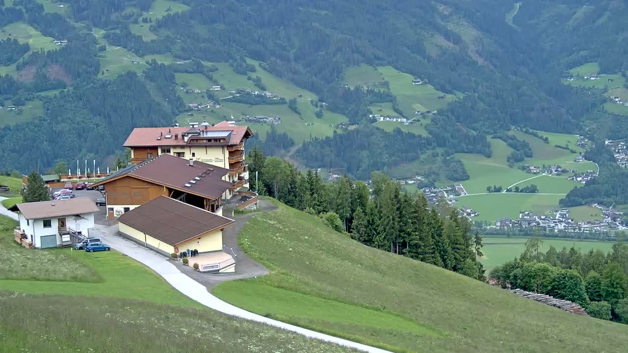 A hillside resort complex overlooks a valley of green fields and a distant village under an overcast sky.