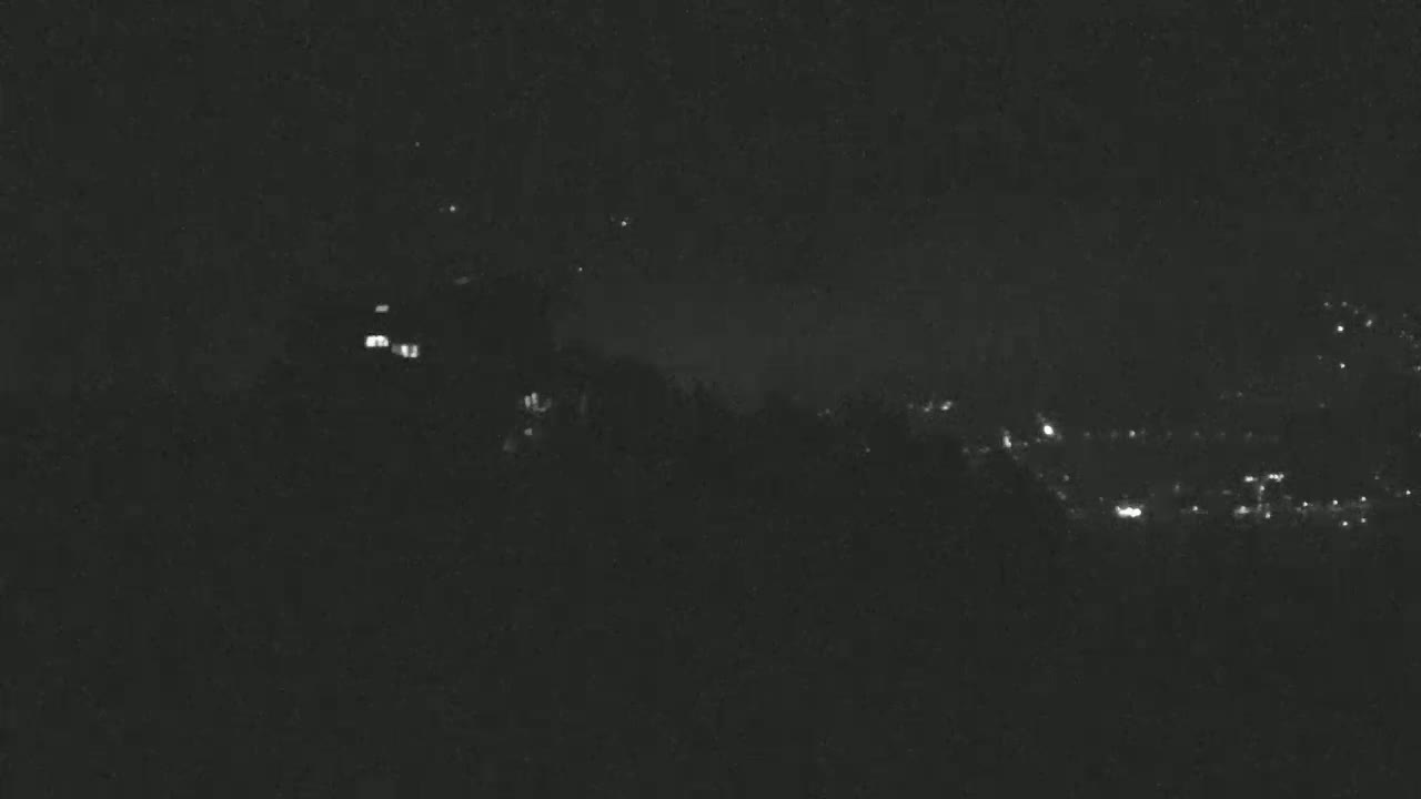 A nighttime view shows a dark hillside with a few distant lights visible below, under a mostly clear sky.