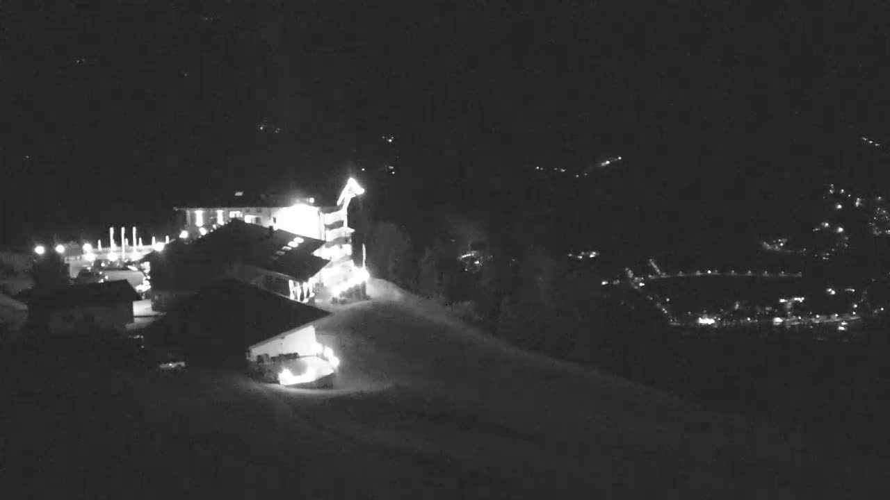 A nighttime, snow-covered hillside shows illuminated buildings and distant lights.