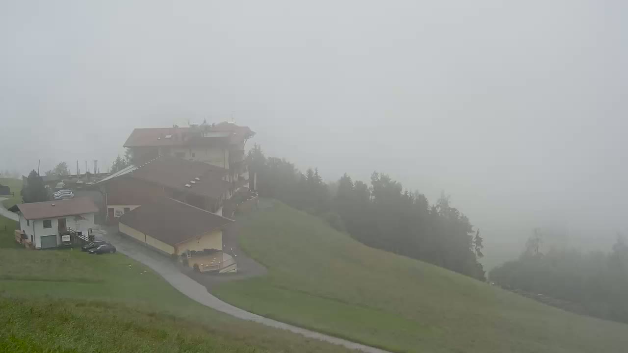 A foggy hillside scene features several buildings, some vehicles, and a paved roadway.