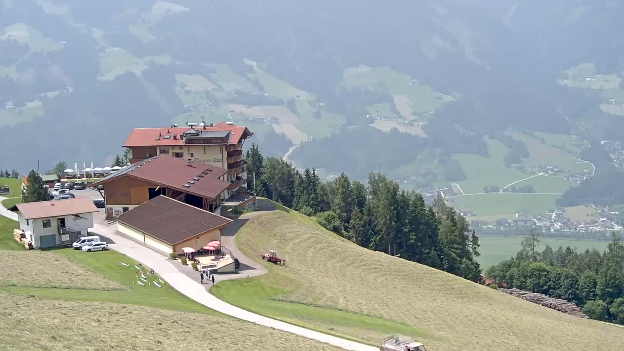 A mountaintop complex of buildings with a paved road leading down to a valley visible in the hazy distance, under sunny conditions.