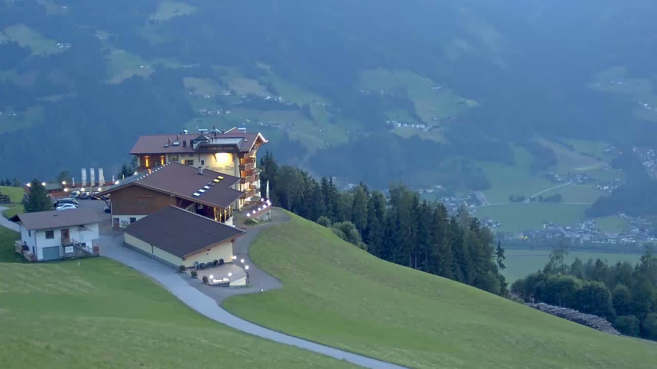 A lighted hotel complex sits atop a grassy hill overlooking a valley shrouded in a hazy twilight.
