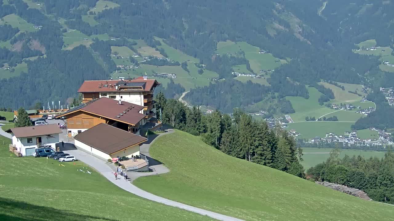 A mountaintop complex of buildings with a parking lot overlooks a valley of green fields and forests on a clear day.