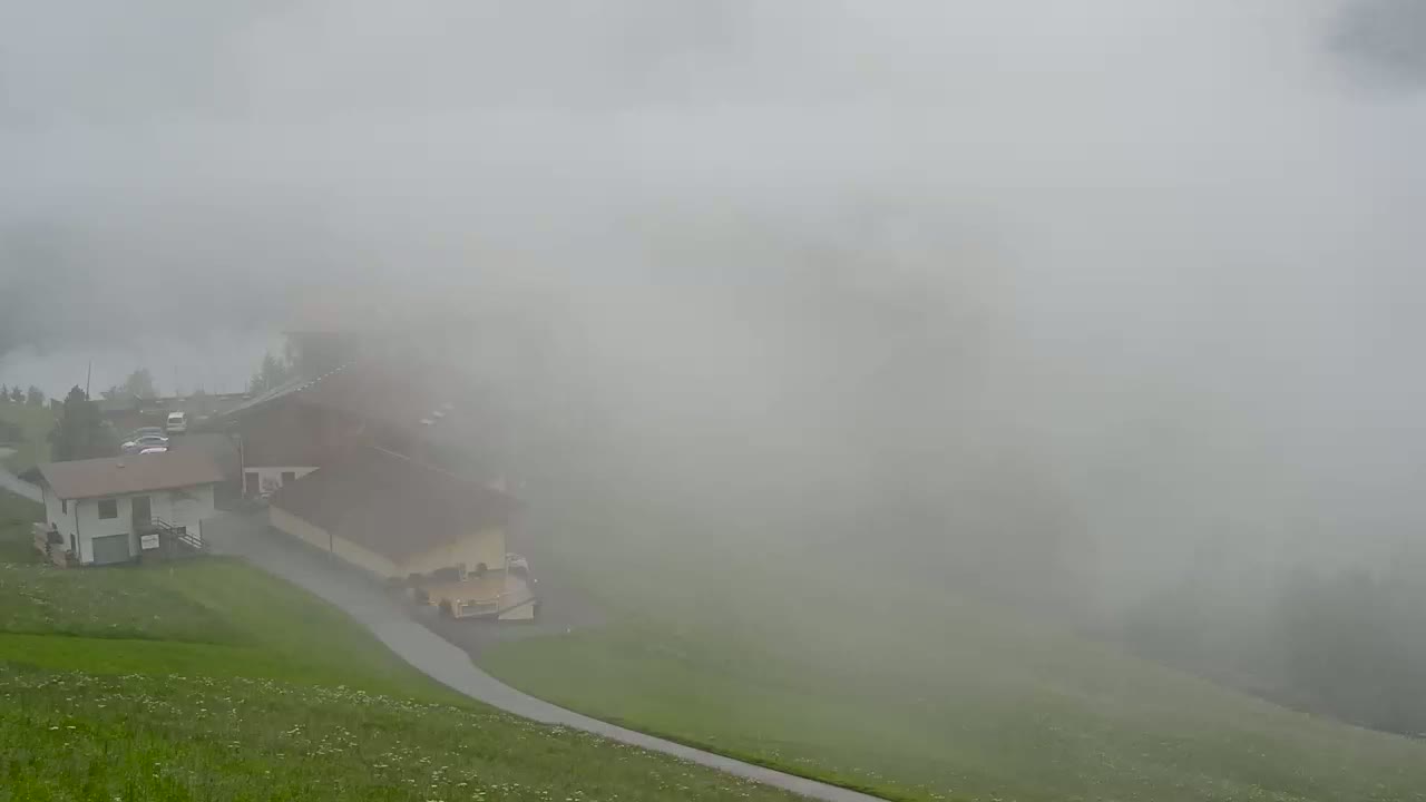 A foggy landscape shows two buildings and a curving road next to a grassy hillside.