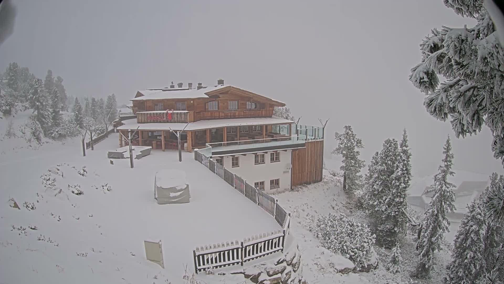 A hillside resort with several buildings and a parking lot overlooks a sprawling valley of green fields and forests under sunny skies.