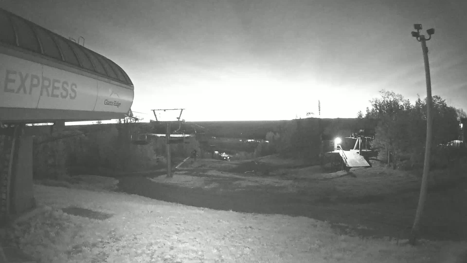 A chairlift's loading area is shown at dusk or dawn, with a snowy landscape extending to a dark horizon.