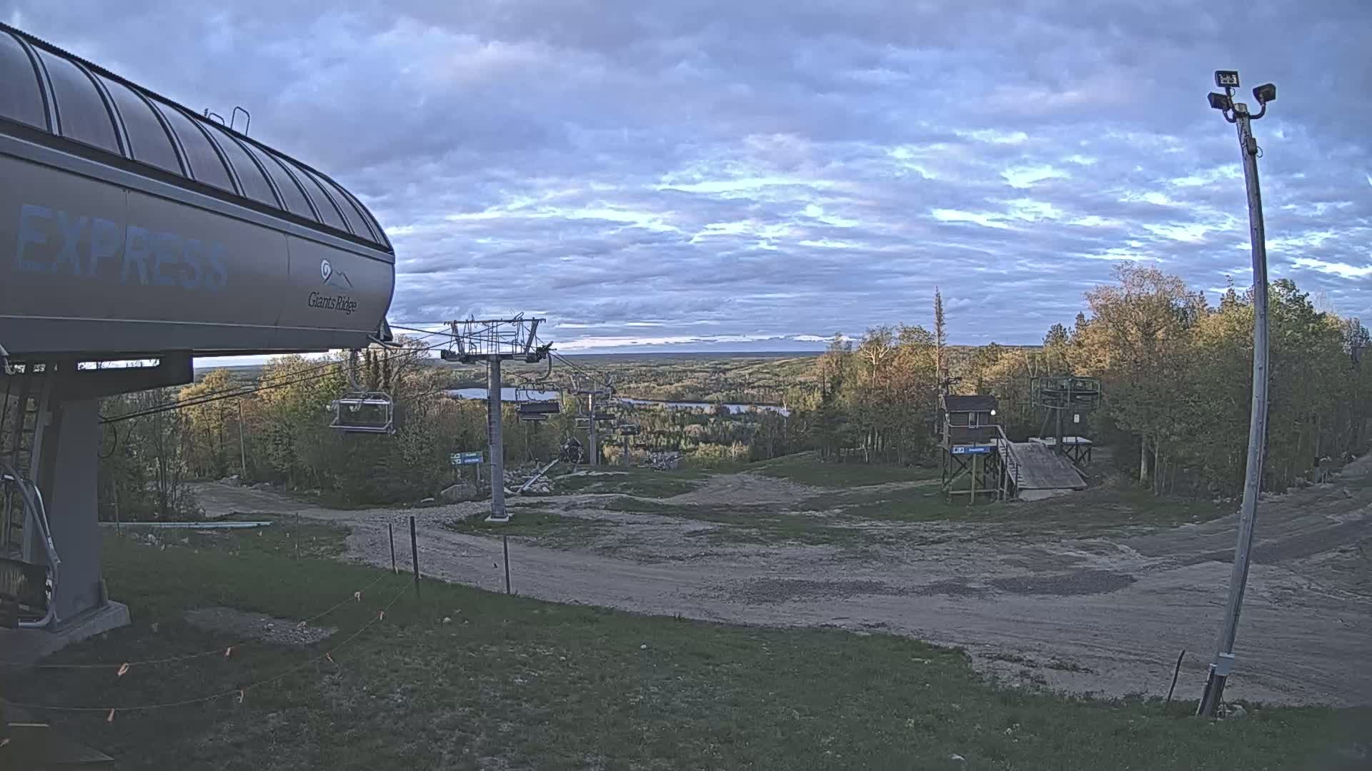 A ski lift and chairlift are visible at the top of a hill overlooking a valley with a cloudy sky.
