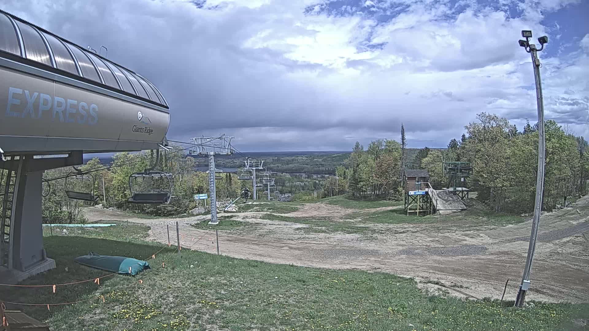 A ski lift base station with a chairlift extending into a wooded area under partly cloudy skies.