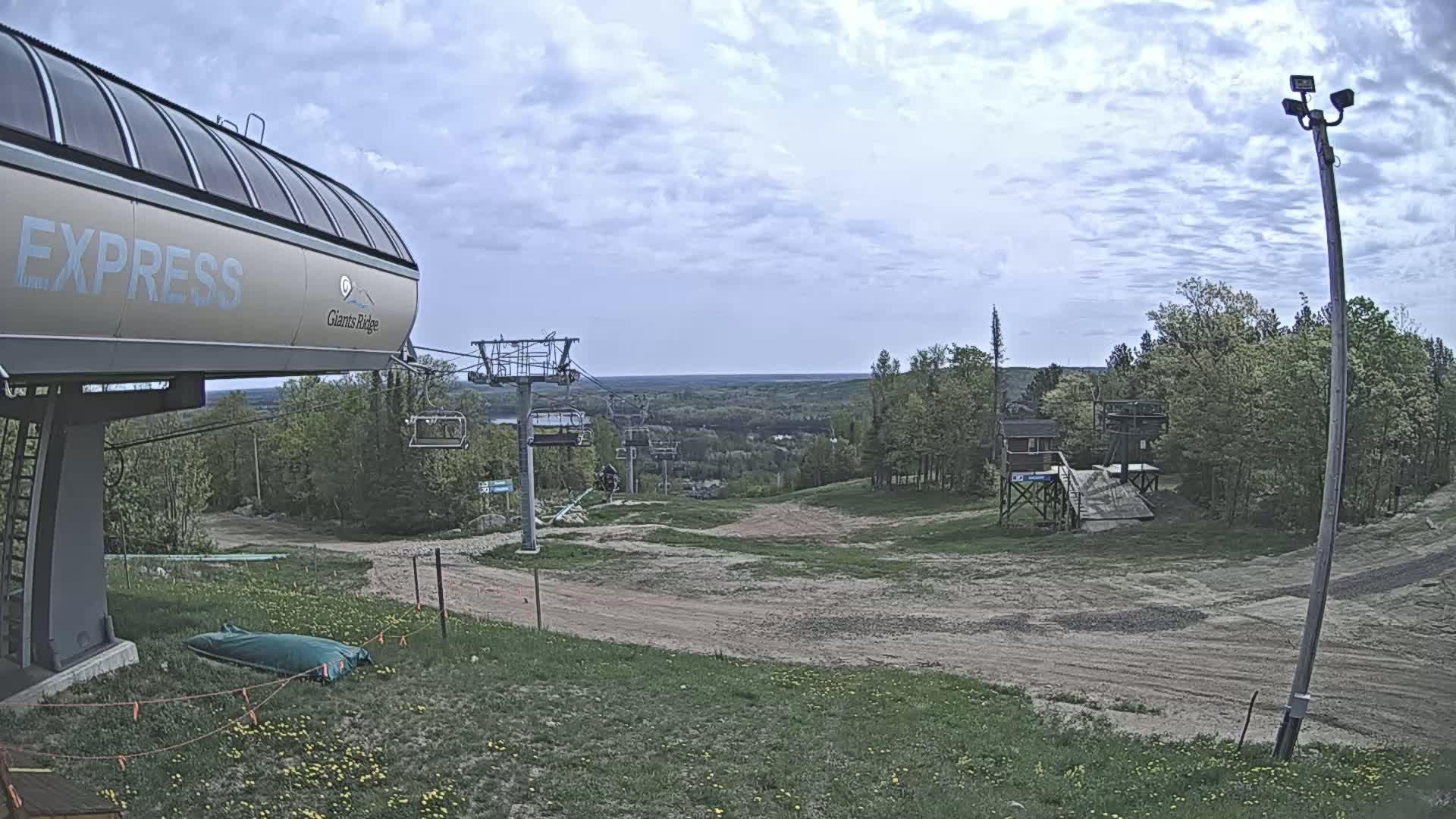 A ski lift base station and chairlift ascending a grassy hill under a partly cloudy sky.
