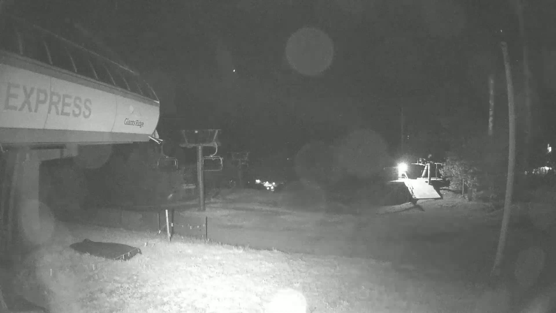 A nighttime, low-light view of a ski lift terminal area with snow on the ground.