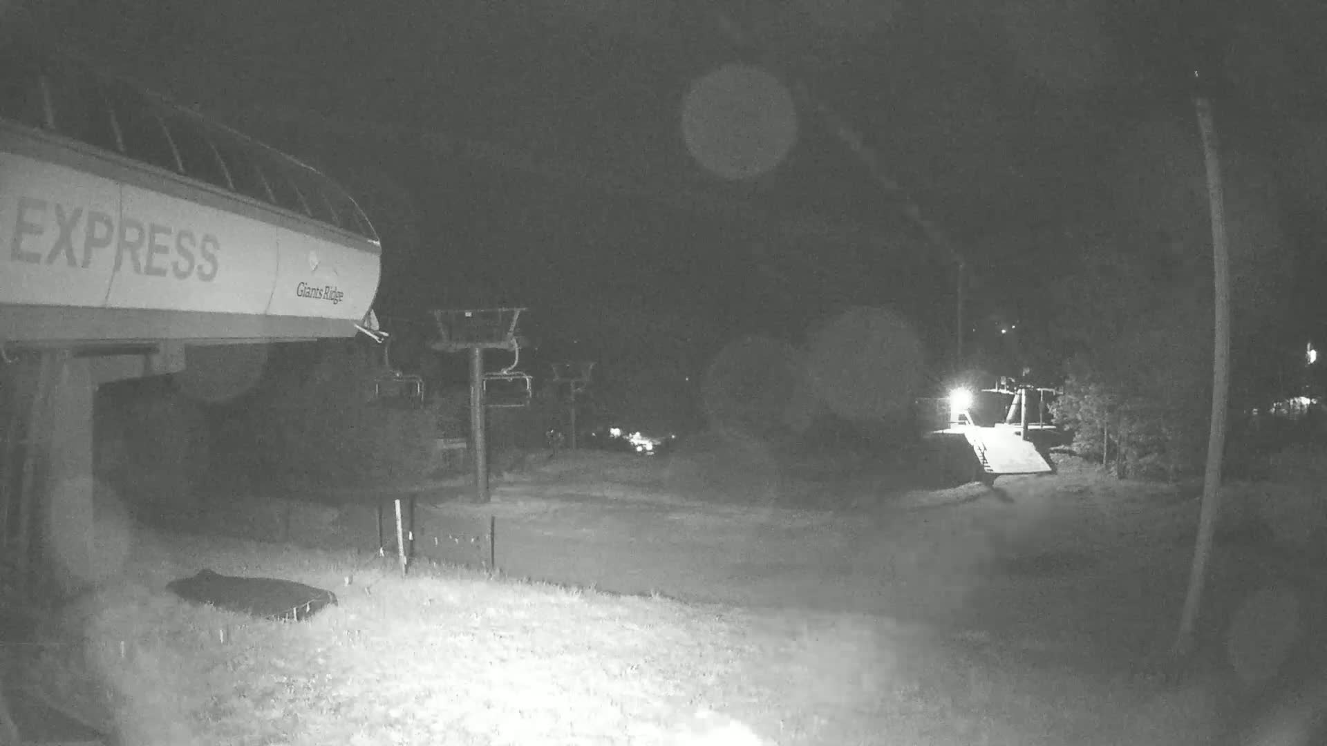 A nighttime, low-light image shows a ski lift and surrounding area with some trees and a ramp.