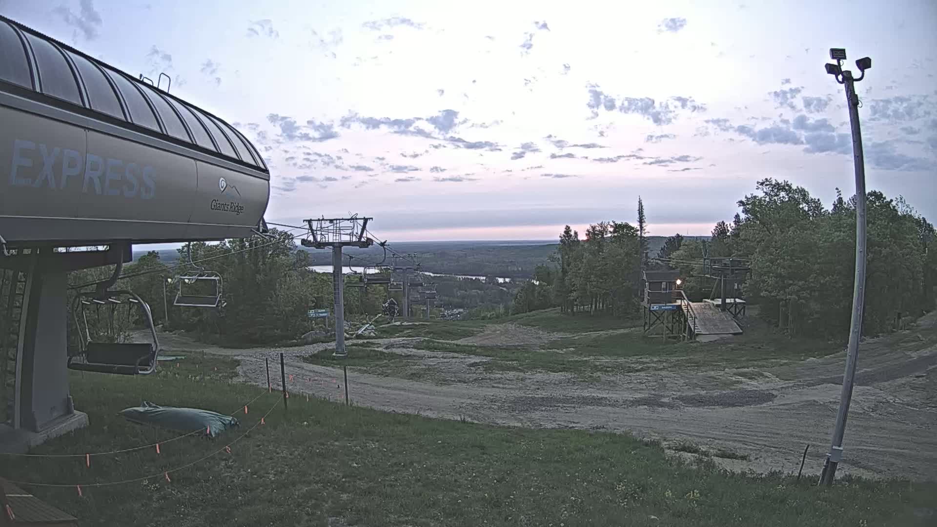 A chairlift at a ski resort overlooks a valley under a partly cloudy, twilight sky.