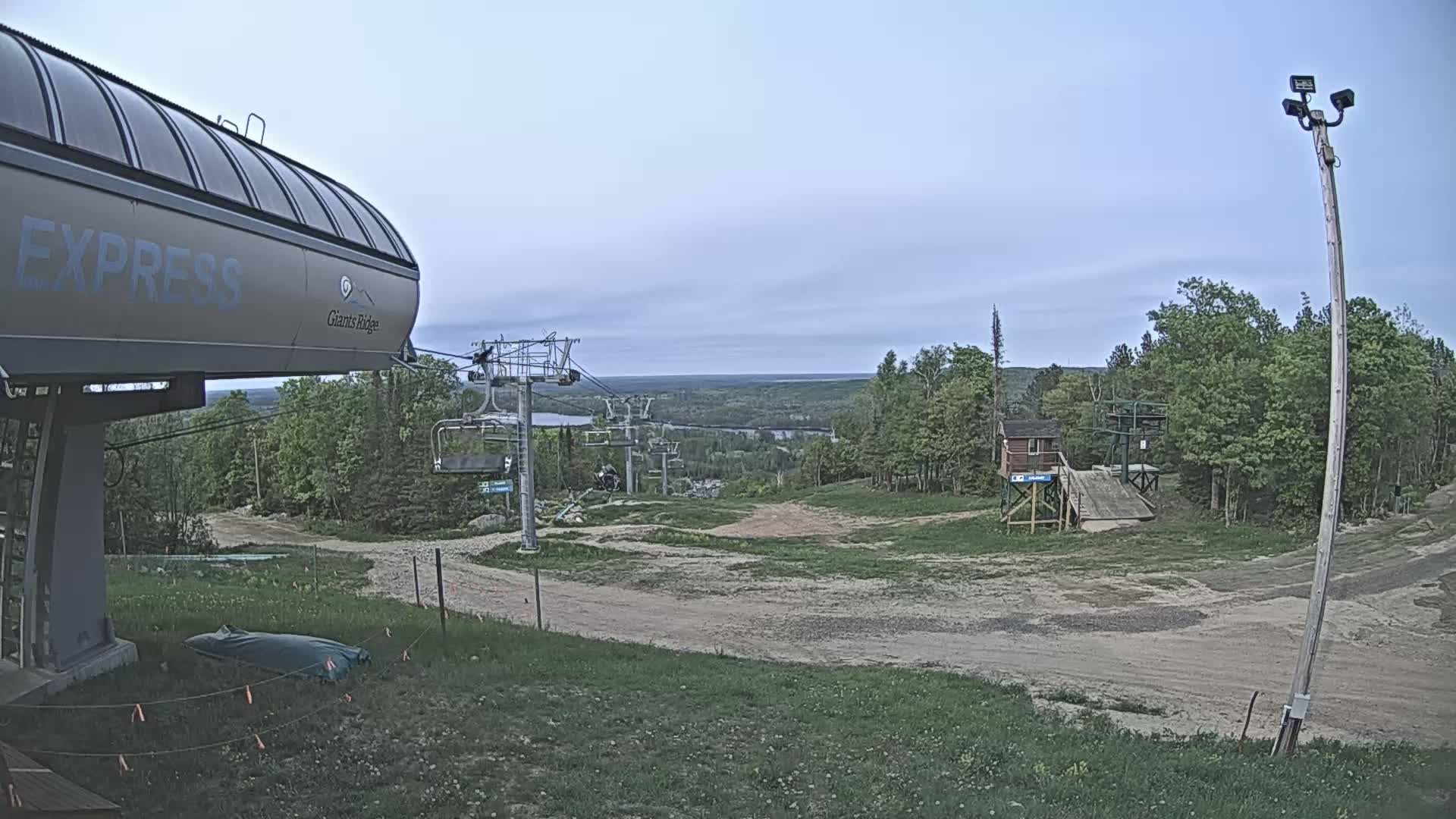 A ski lift base station with a chairlift extending into a forested area under an overcast sky.
