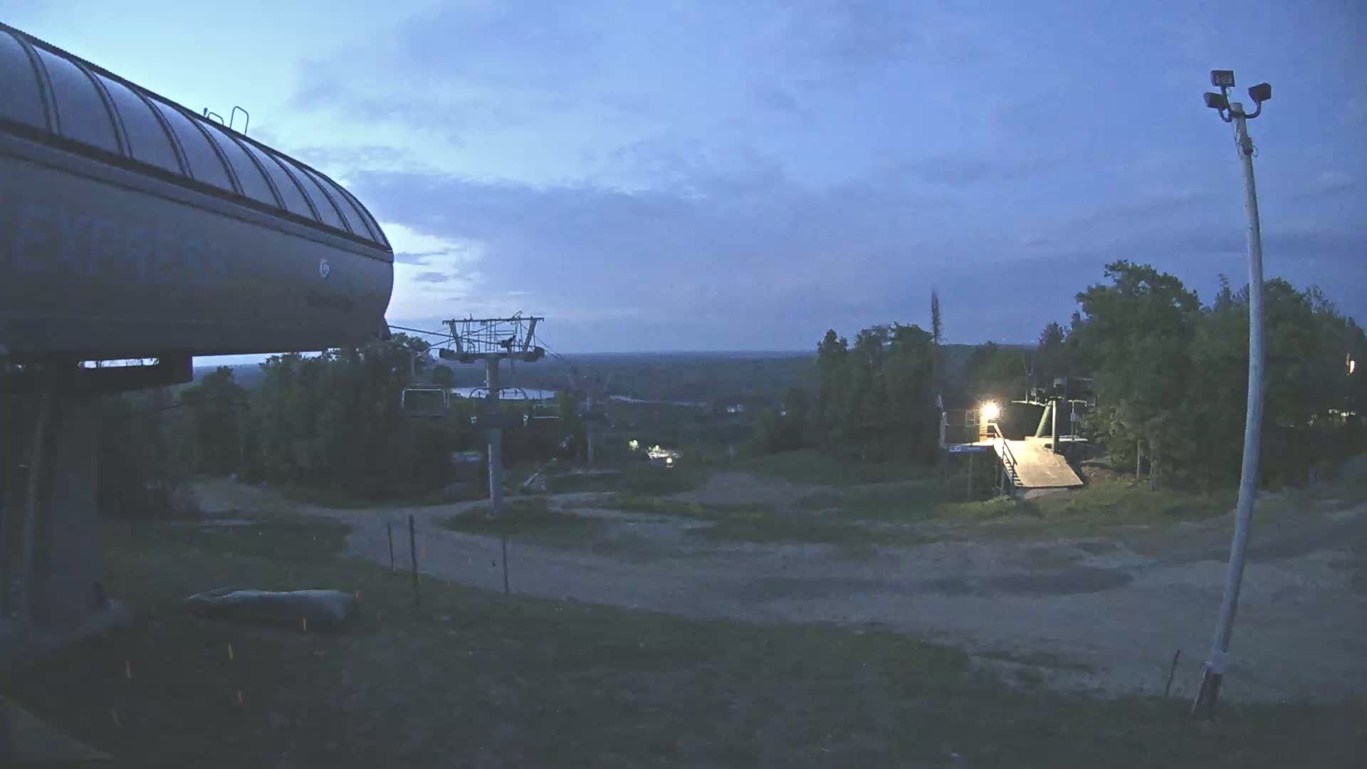 A ski lift and a portion of a ski resort are visible at dusk under a cloudy sky.