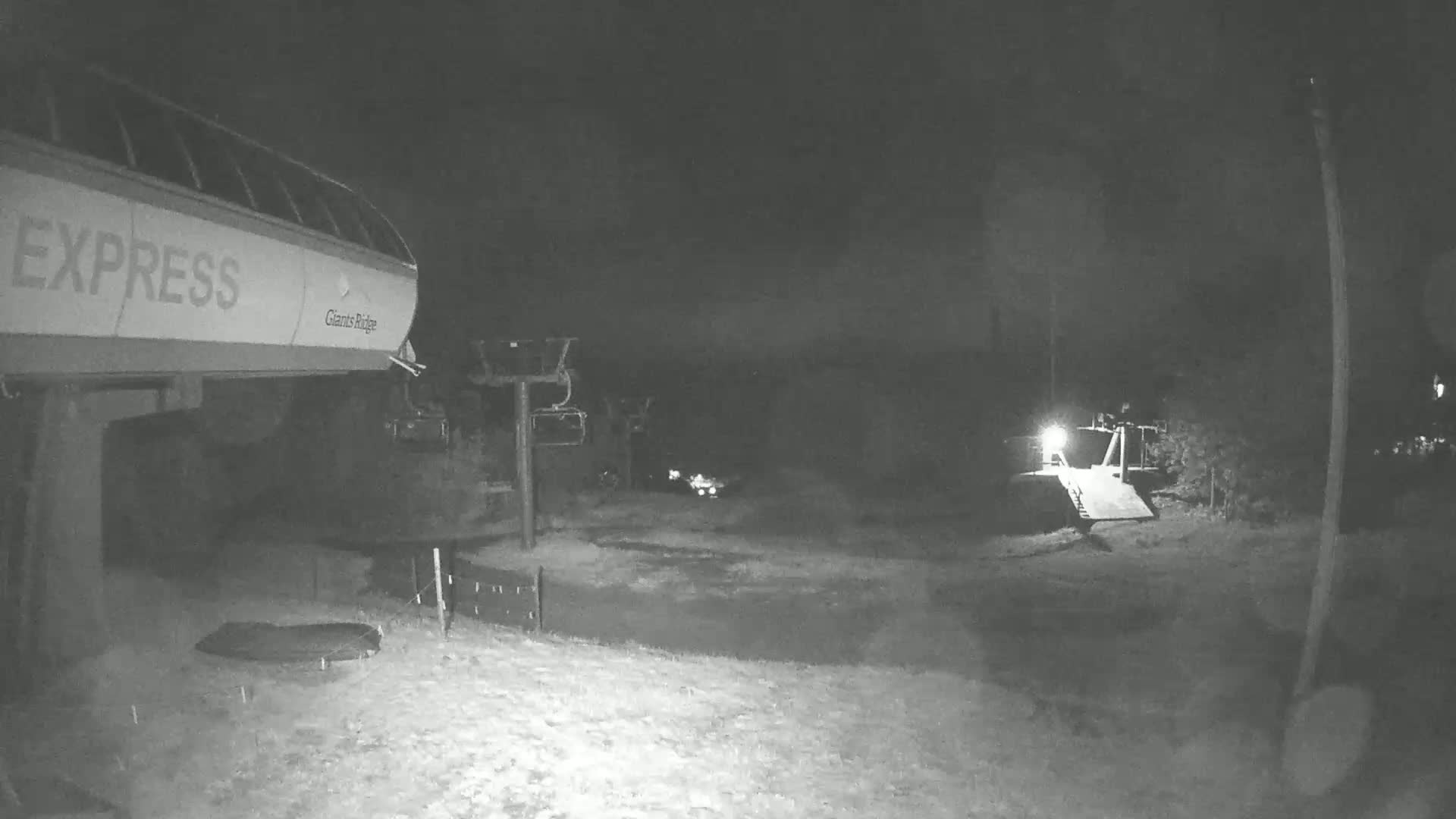 A nighttime, snow-covered ski lift area with a chairlift and the word "EXPRESS" visible on the side of a lift structure.
