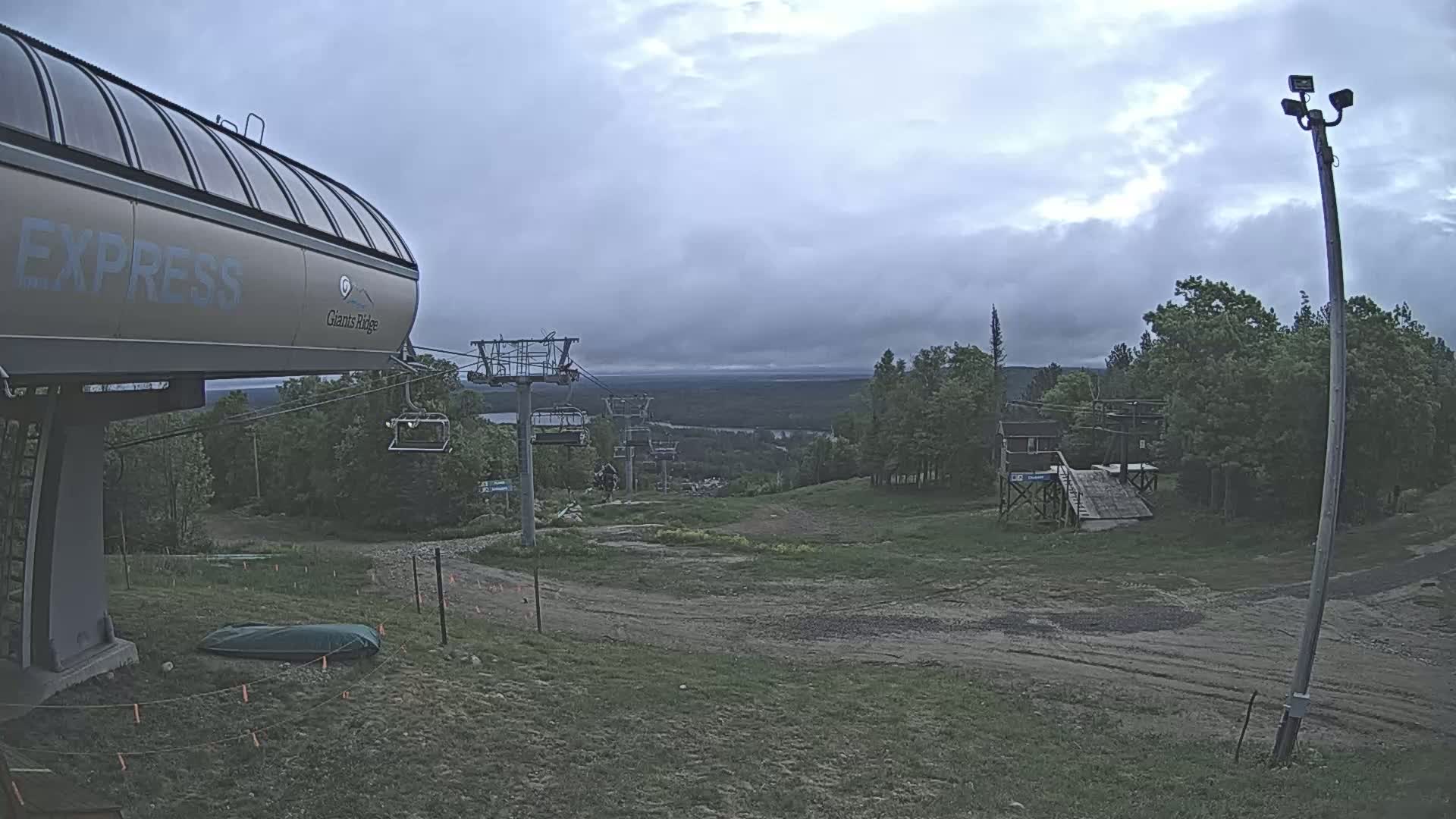 A chairlift and a grassy hill with trees and a cloudy sky are visible.