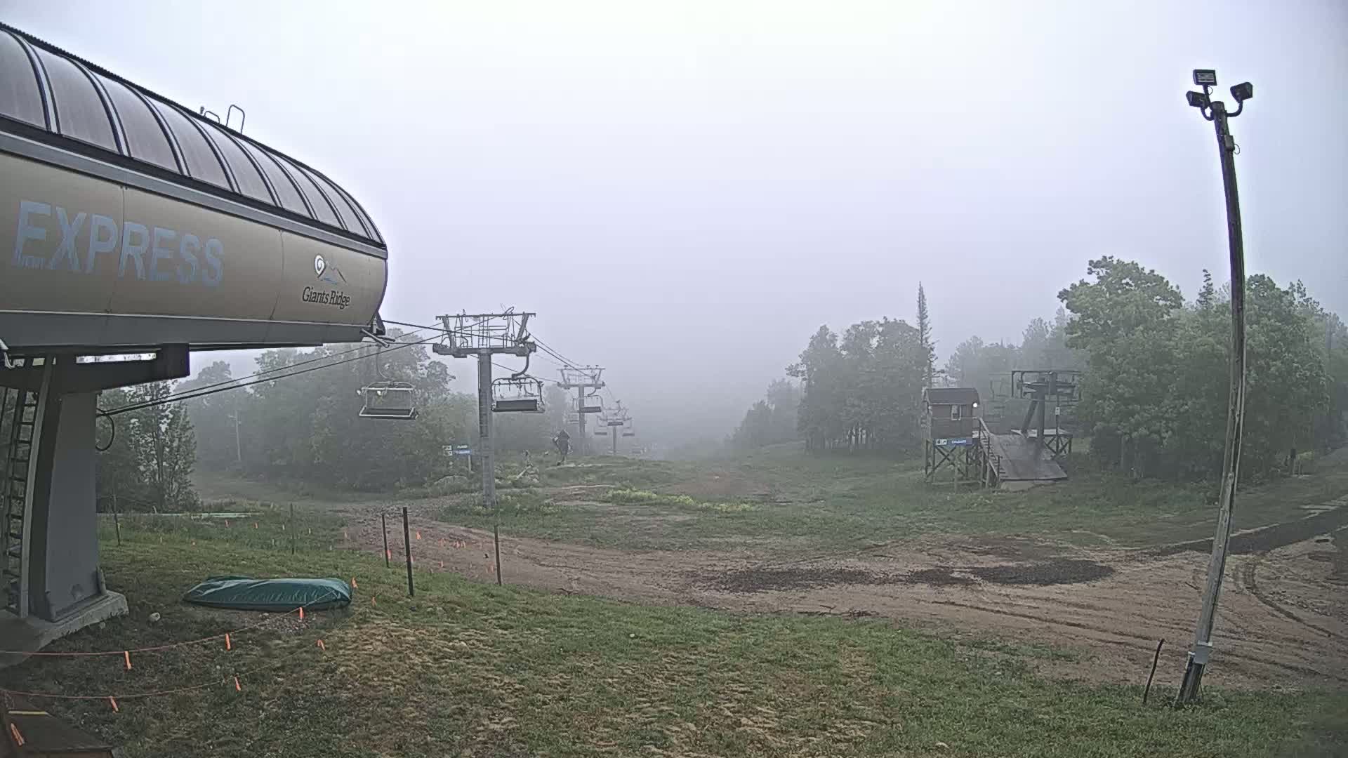 A chairlift extends into a foggy landscape of grassy hills and trees.