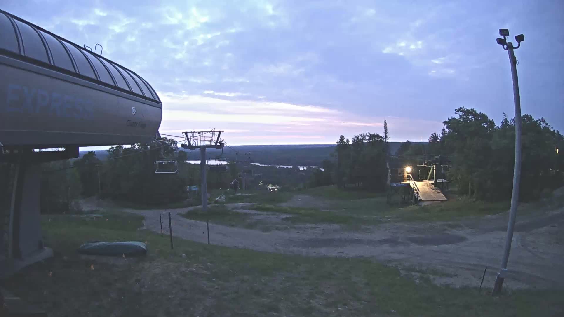 A ski lift base station at dusk, overlooking a valley under a partly cloudy sky.