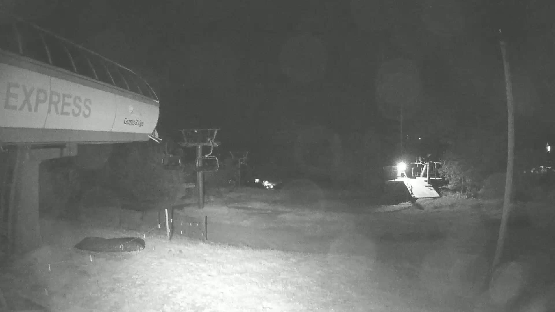 A nighttime, low-light view shows a chairlift labeled "Express" and a ski lift in a snow-covered area.