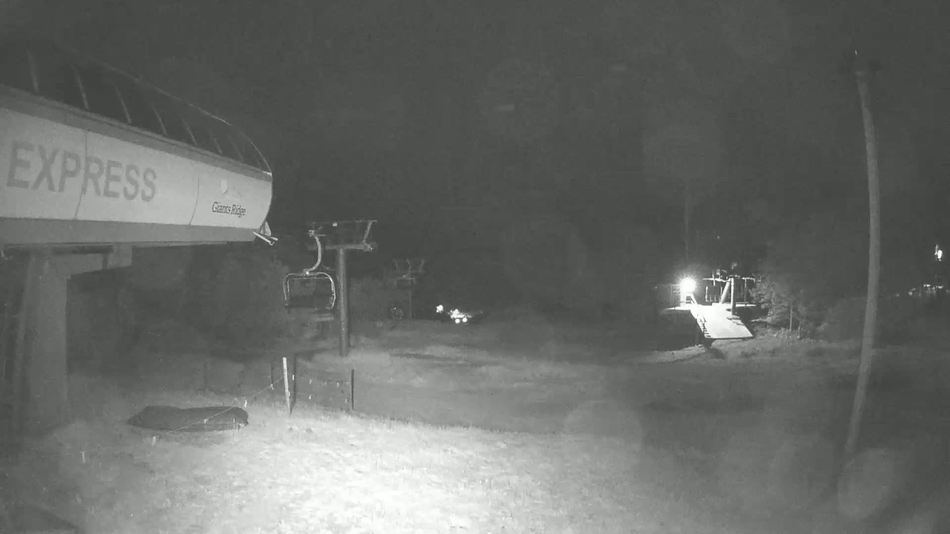 A nighttime, low-light view of a ski lift base area with a chairlift and an Express gondola.