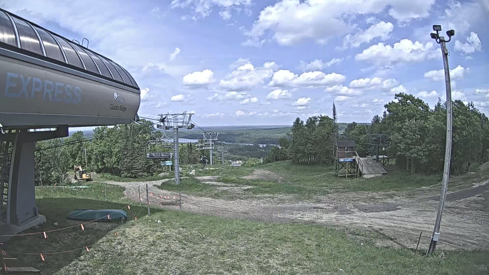 A ski lift base station with a chairlift extending into a grassy hillside under a partly cloudy sky.