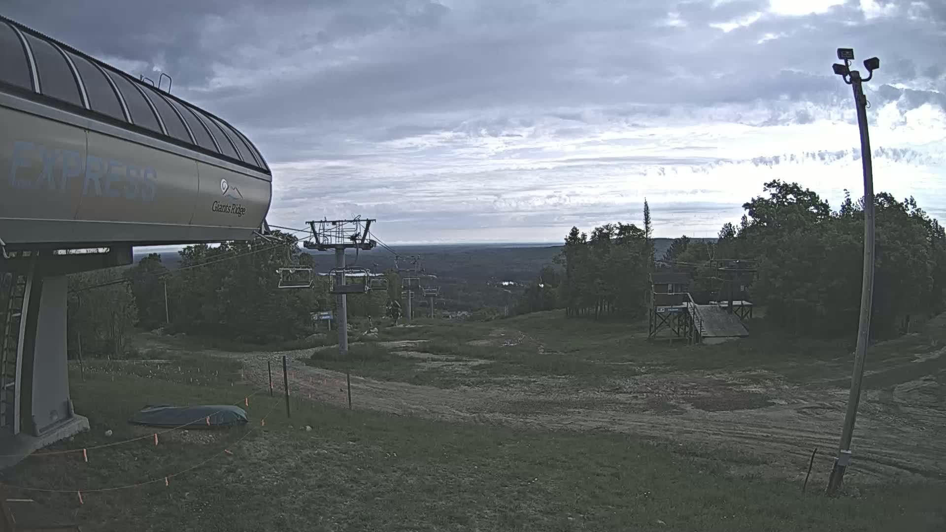 A ski lift base station with overcast skies and a distant view of forested hills under a cloudy sky.