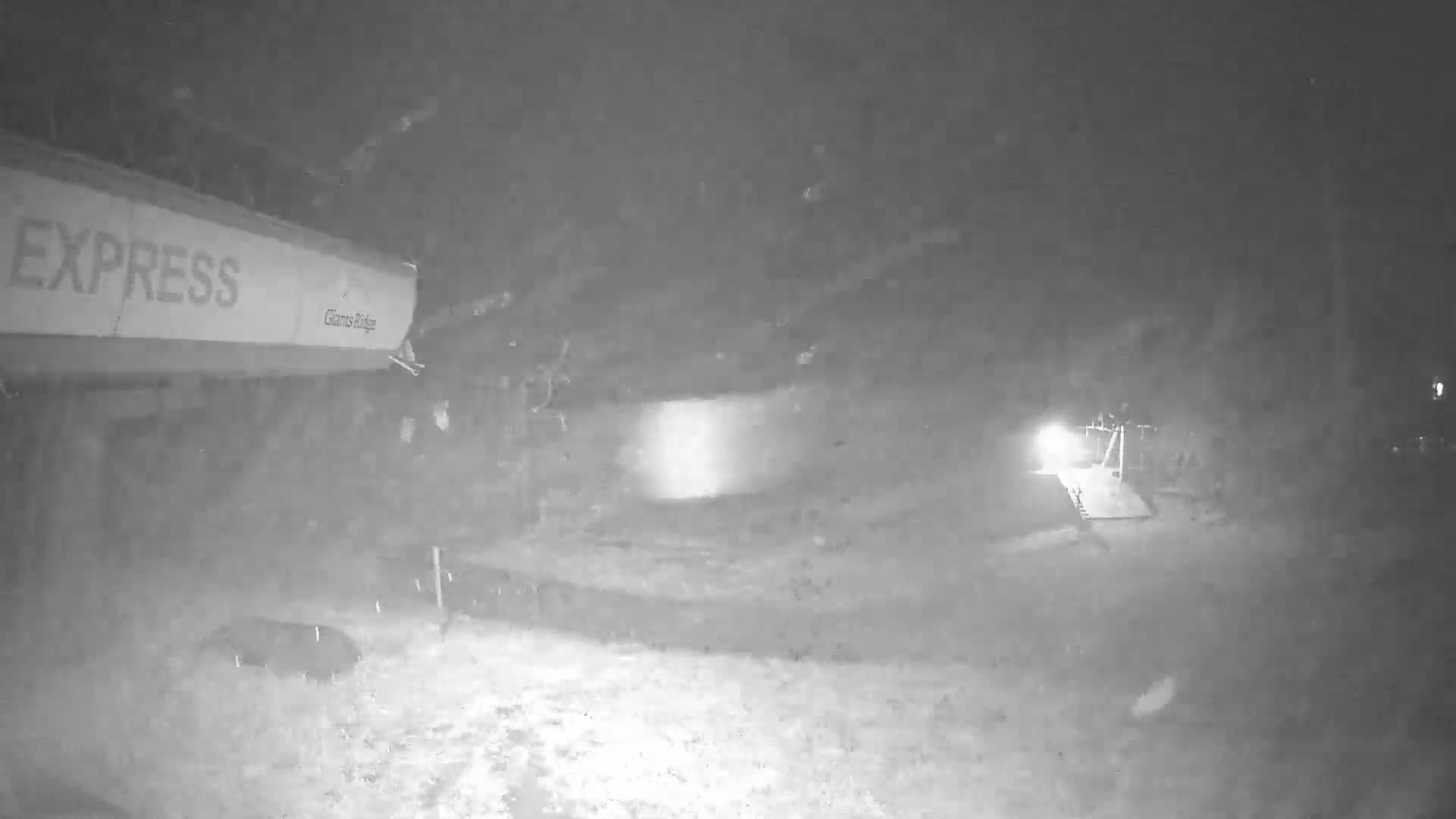 A nighttime, snowy scene shows part of a ski lift and a snow-covered ground.
