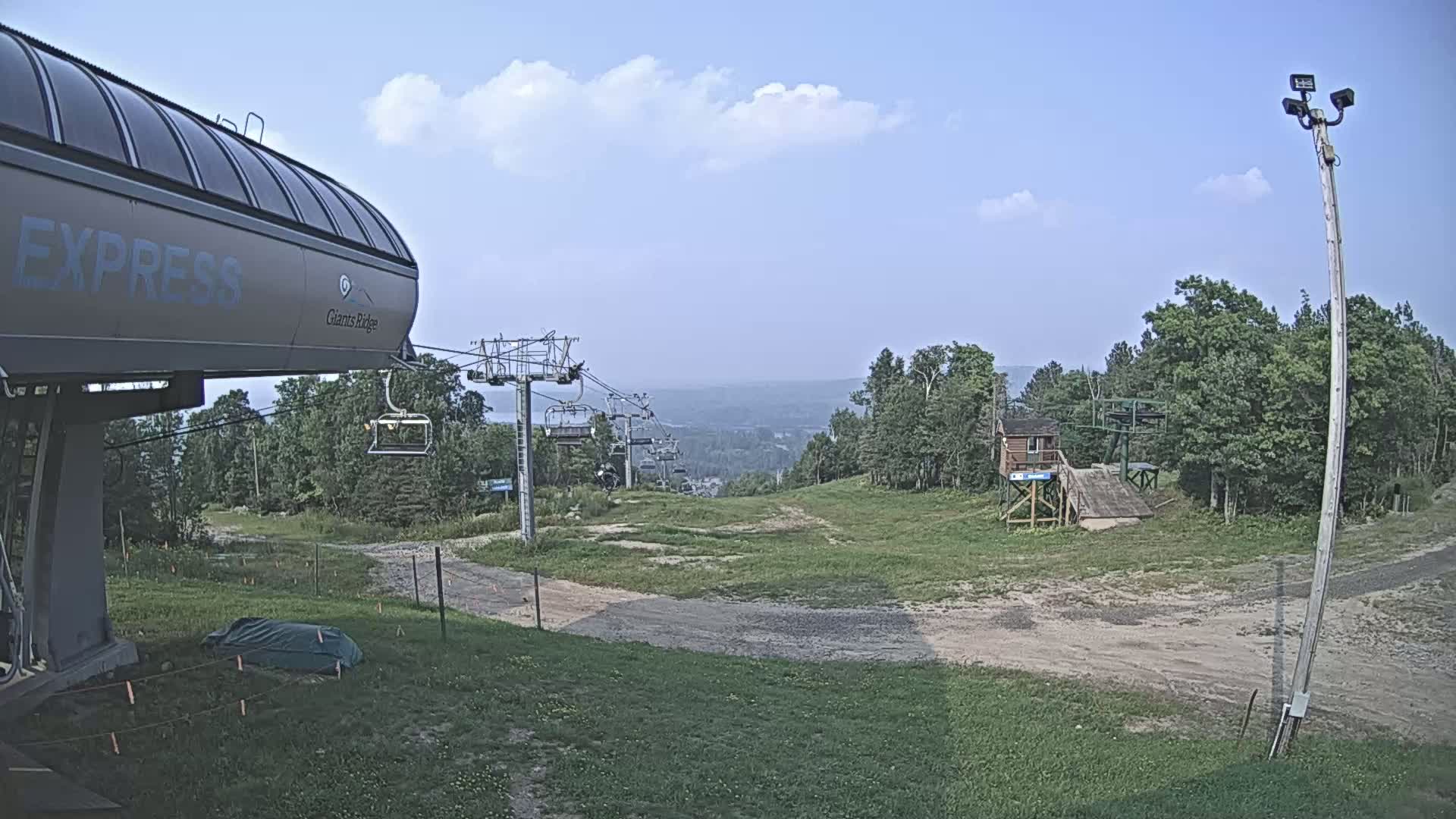 A nighttime, snow-covered ski lift base area with a chairlift in the foreground and other lifts and structures visible in the distance under a moonlit sky.