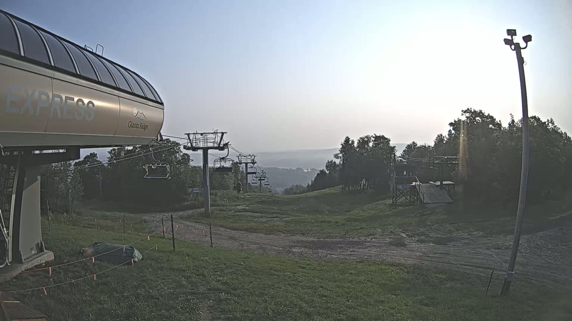 A nighttime, snow-covered ski lift base area with a chairlift in the foreground and other lifts and structures visible in the distance under a moonlit sky.