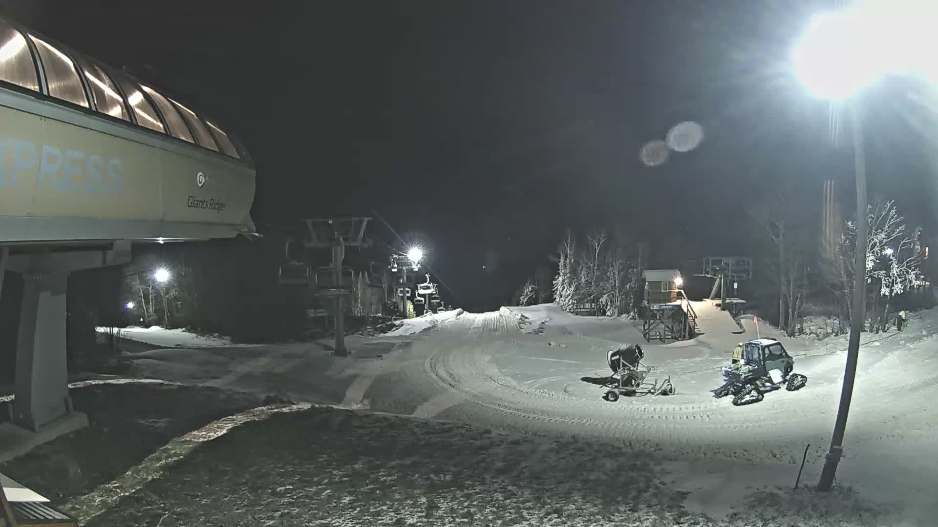 A nighttime, low-light view of a ski lift and surrounding snowy ground.